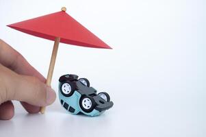 Red toy umbrella and upside down car on white background. Insurance coverage concept photo