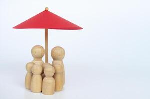 Red toy umbrella and wooden family doll figures a white background. Life insurance coverage concept photo