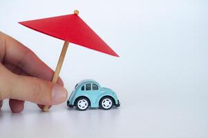 Red toy umbrella and blue toy care on white background. Car insurance coverage concept photo