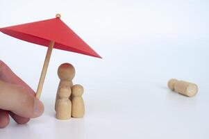 Family wooden dolls covered with toy umbrella representing life insurance and family protection photo