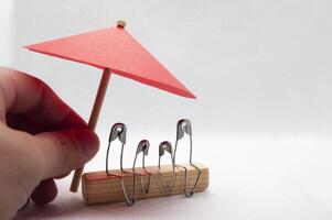 Model safety pin of family sitting on wooden block with red umbrella background. Insurance concept photo