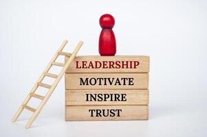 Leadership, motivate, inspire and trust text on wooden blocks with wooden red doll and ladder. photo