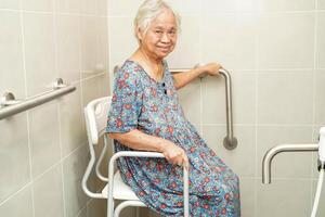 Asian elderly old woman patient use toilet support rail in bathroom, handrail safety grab bar, security in nursing hospital. photo