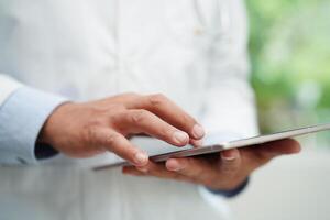 asiático hombre médico utilizando tableta computadora a leyendo paciente informe, cheque arriba y buscar para resolver tratamiento salud médico en línea en hospital. foto