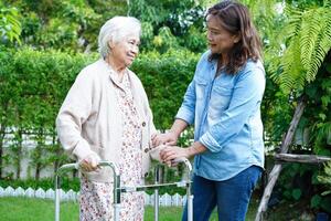 cuidador ayuda a una anciana asiática con discapacidad a caminar con un caminante en el parque, concepto médico. foto