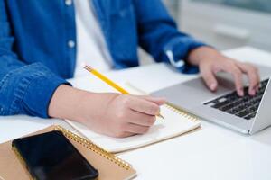 asiático Adolescente estudiante escribir deberes con ordenador portátil computadora, aprendizaje Universidad educación concepto. foto