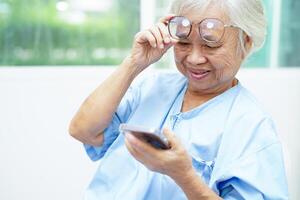 Asian senior woman wearing eyeglasses or vision glasses using a smartphone at home care service. photo