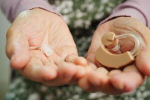 Asian senior woman patient using hearing aid in ear to reduce hearing loss problem. photo