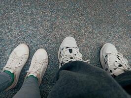 Selfie of man and woman legs in white sneakers standing on the floor photo