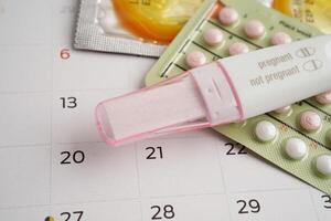 Pregnancy test with birth control pills and condom for female on calendar, ovulation day. photo