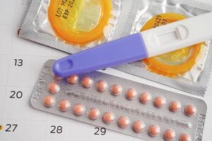 Pregnancy test with birth control pills and condom for female on calendar, ovulation day. photo