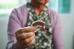 Asian senior woman patient using hearing aid in ear to reduce hearing loss problem. photo