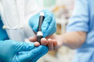 Asian doctor using lancet pen on senior patient finger for check sample blood sugar level to treatment diabetes. photo