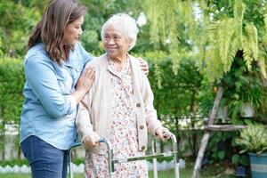 Doctor help Asian elderly woman disability patient walk with walker in park, medical concept. photo