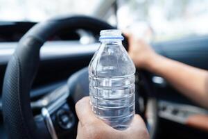 Asian woman driver hold cold water for drink in car, dangerous and risk an accident. photo