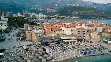 playa con Dom paraguas cerca el Roca fortaleza paredes de el antiguo pueblo de Budva. montenegro zumbido foto