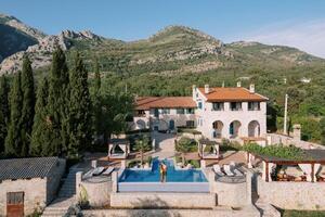 Man and woman stand hugging and kissing on the edge of a swimming pool near an old villa at the foot of the mountains photo