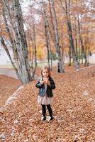 Little girl with an apple in her hand stands thinking in the autumn forest photo