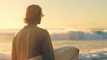 een Mens staat Aan een zanderig strand, Holding een surfboard onder zijn arm, klaar voor een dag van surfing in de oceaan. video