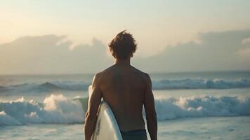 een Mens staat Aan de zanderig strand, Holding een surfboard in zijn handen, klaar voor een dag van surfing in de oceaan. video