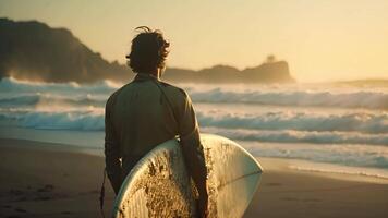 een Mens staand Aan de zanderig strand, Holding een surfboard onder zijn arm. video
