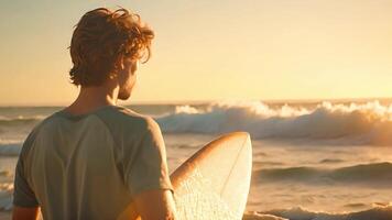 een Mens staat Aan een strand Holding een surfboard onder zijn arm. video