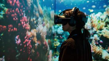 A person wearing a virtual reality headset stands in front of a vibrant wall of corals, exploring a digital underwater world. video