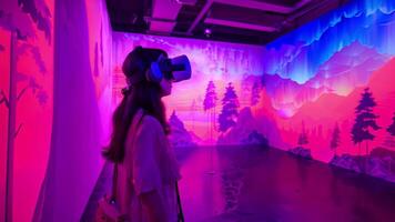 A woman stands immersed in a vibrant, illuminated art exhibit while wearing a virtual reality headset. video