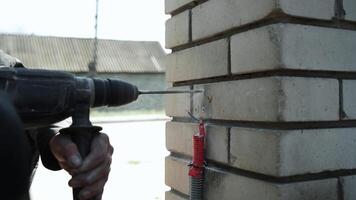 constructor simulacros un agujero en el pared con un martillo perforar. de cerca de martillo perforar perforador haciendo agujero video