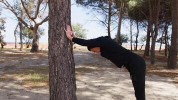 Mens met zwart trainingspak strekt zich uit in een pijnboom boom video