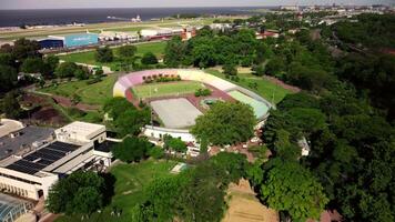 Aerial drone view of green sports stadium in city landscape. Outdoor court, park with trees, streets, modern urban architecture. Top view of summer cityscape, recreation area, nobody playing. video