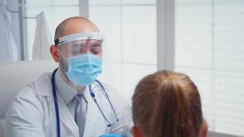 Close up of doctor with visor checking temperature. Physician specialist in medicine with mask providing health care services consultation treatment examination in hospital cabinet during covid-19 video