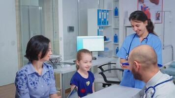 Doctor and nurse talking with child patient sitting at desk in medical office. Healthcare physician specialist in medicine providing health care services radiographic treatment examination in hospital video