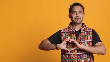 Portrait of smiling loving man doing heart symbol shape gesture with hands, showing kindness. Happy affectionate person doing tender love gesturing, isolated over studio background, camera A video