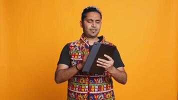 Man shakes head in disbelief after realizing lack of necessary funds while trying to shop online on tablet. Disappointed indian person gets credit card transaction rejected, studio backdrop, camera B video