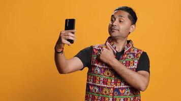 Indian narcissistic man using cellphone to take selfies from all angles. Vain social media user taking photos using phone selfie camera, smiling happily, studio background, camera A video