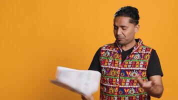 Indian man browsing though financial audit report files, throwing them in anger, feeling overworked, studio background. Stressed worker annoyed by paperwork, refusing to work anymore, camera A video