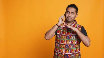 Happy man in traditional clothing chatting with best friend over telephone call. Upbeat person with colorful attire communicating with mate using phone, studio background, camera B video