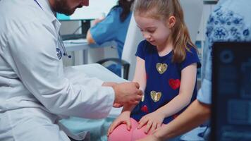 Little girl having arm bandaged sitting in bed during consultation. Healthcare physician specialist in medicine providing health care service radiographic treatment examination in hospital cabinet video