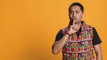 Annoyed indian man doing shushing hand gesturing, irritated by noise, having negative mood. Person placing finger on lips, doing quiet sign gesture, studio background, camera A video