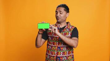 Content creator in traditional clothing recommending isolated screen phone, studio backdrop. Indian man reviewing copy space mockup smartphone device for online tech channel, camera B video