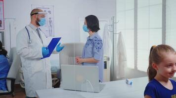 Parent and doctor talking in madical office wearing protective mask during covid-19 pandemic. Physician specialist in medicine providing health care services consultation treatment in hospital cabinet video