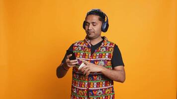 Joyous man listening music, having fun dancing, enjoying hot beverage. Upbeat person wearing headphones, doing funky movements, drinking coffee, studio background, camera B video