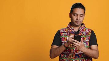 Indian man adding payment method on mobile phone website, purchasing stuff, isolated over studio background. Client does internet shopping, typing debit card info on cellphone, camera A video