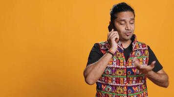 Man discussing with best friend over telephone call, enjoying leisure time. Upbeat person wearing indian attire talking with mate in phone call, isolated over studio backdrop, camera A video