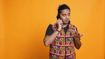 Man discussing with best friend over telephone call, enjoying leisure time. Upbeat person wearing indian attire talking with mate in phone call, isolated over studio backdrop, camera B video