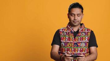 indisch Mann spielen Videospiele auf Handy im Landschaft Modus, genießen Freizeit Zeit. Spieler genießen Spiel auf Handy, Mobiltelefon Telefon, haben Spaß, isoliert Über Studio Hintergrund, Kamera ein video