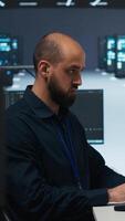 Vertical Engineer writing code in high tech facility with server rows providing computing resources for different workloads. Trucking right shot of employee overseeing supercomputers operating data video