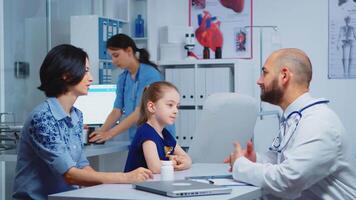 Child and doctor talking in clinic while nurse checking pills. Pediatrician specialist in medicine providing health care services consultation diagnostic examination treatment in hospital cabinet video
