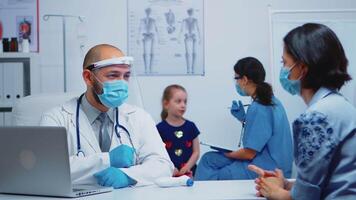 Doctor talking with parent while nurse consulting child wearing protection mask. Physician specialist in medicine providing health care services consultation treatment examination in hospital cabinet. video